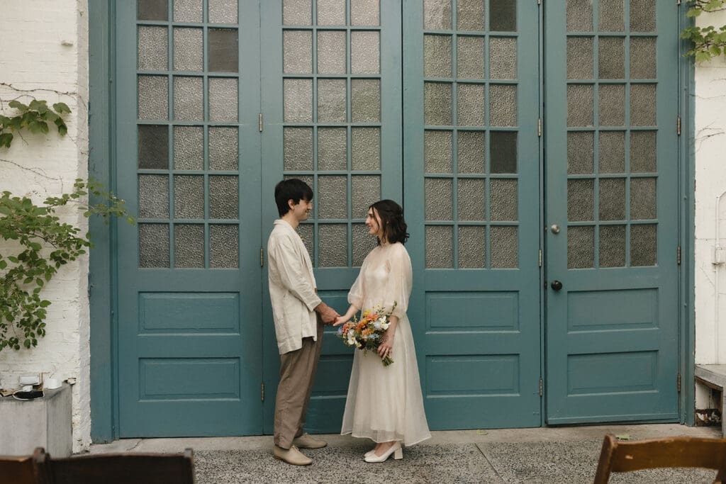 Bride and groom who got married at the MAAS Building in Philadelphia hold hands in front of a set of teal French doors