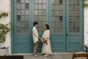 Bride and groom who got married at the MAAS Building in Philadelphia hold hands in front of a set of teal French doors