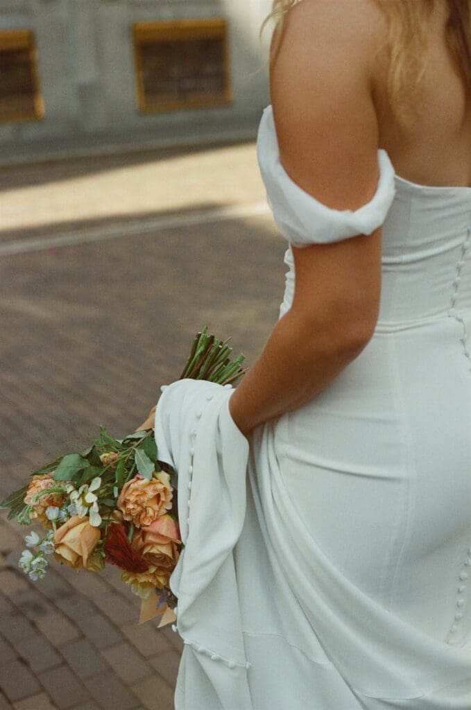 Closeup detail image on film of bride with her fall floral bouquet in her hand with her wedding dress train draped over her arm