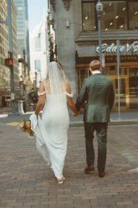 Film image of bride and groom crossing a brick paved crosswalk in front of Eddie V's restaurant during their Pennsylvania wedding portraits
