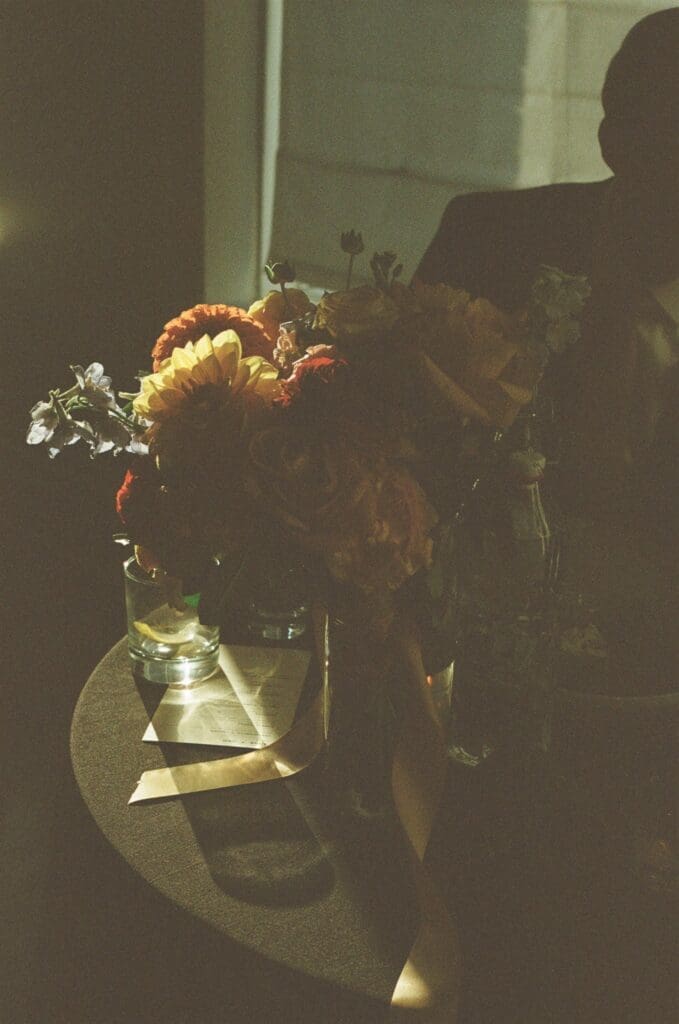 Grainy film image of a warm toned floral bouquet sitting on a table with sun rays filtering in behind it