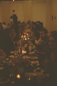 Moody film image of a long banquet table full of wedding guest eating, drinking, talking and laughing during an intimate indoor wedding in Pennsylvania