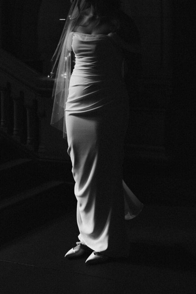 Black and white silhouette of bride in a fitted off-shoulder crepe gown and pearl-edged veil standing in a darkened corridor inside Allegheny County Courthouse in Pittsburgh — editorial bridal portrait by Pennsylvania wedding photographer Shiloh Leath
