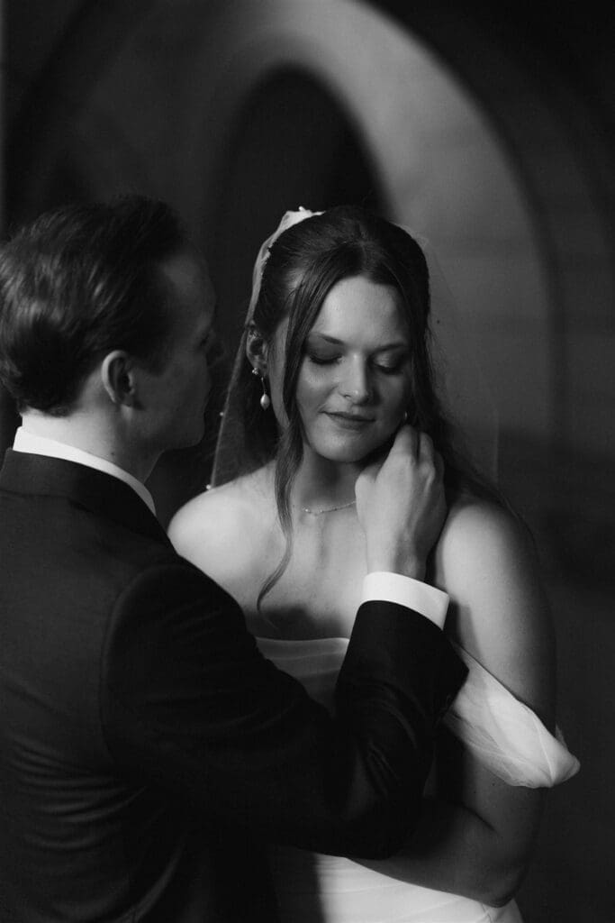 Black and white intimate wedding portrait of groom touching bride's face as she looks down with eyes closed — moody, film-like couple portrait taken inside Allegheny County Courthouse in Pittsburgh, shot by Shiloh Leath Photography
