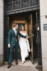 Bride and groom stepping through the ornate iron entry doors of Allegheny County Courthouse in downtown Pittsburgh, Pennsylvania — candid just-married moment captured in warm natural light