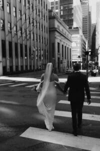 Black and white documentary wedding portrait of bride and groom crossing a street in downtown Pittsburgh, Pennsylvania — veil trailing in motion, shot in a film-inspired editorial style by Shiloh Leath Photography