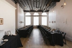 Union Hall at Bar Marco reception room set for an intimate Pittsburgh wedding — long family-style tables with black linens, arched windows, and an ornate painted tin ceiling in the Strip District