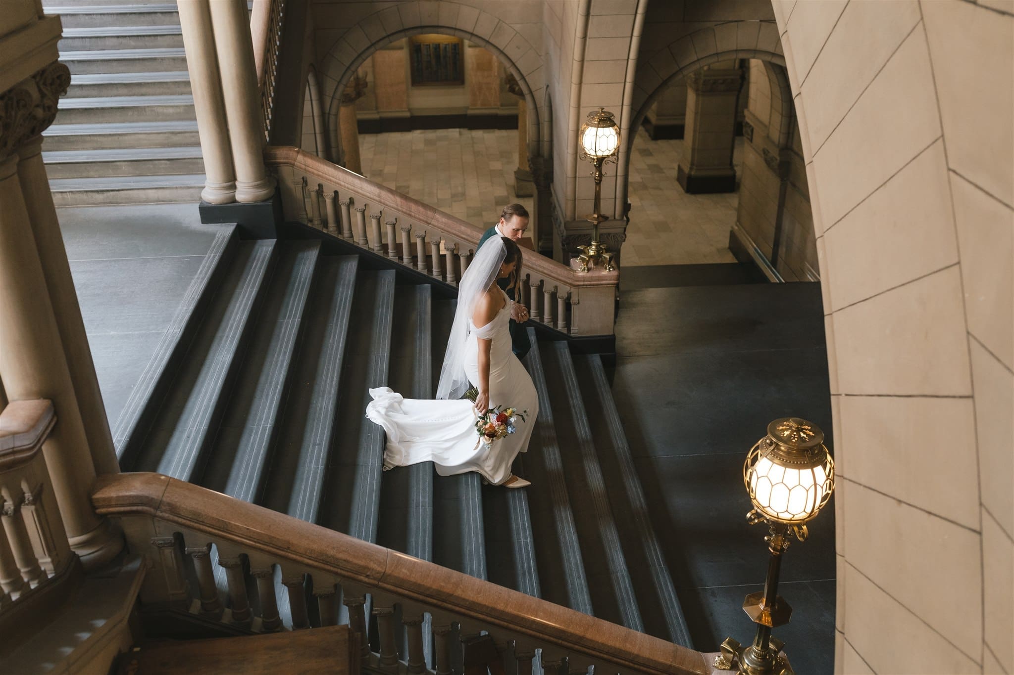 Overhead view of a bride and groom descending the Grand Staircase at Allegheny County Courthouse in Pittsburgh, Pennsylvania — bride's cathedral train trailing behind her, shot on digital by Philadelphia wedding photographer Shiloh Leath