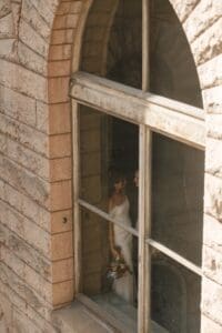Bride standing inside an arched stone window of the Allegheny County Courthouse in Pittsburgh, Pennsylvania, bouquet in hand — editorial bridal portrait with warm natural light and aged limestone exterior