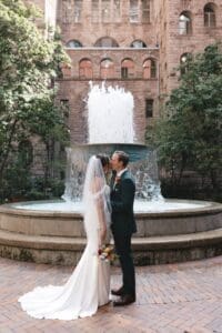 Bride and groom sharing their first kiss in front of the stone fountain courtyard at Allegheny County Courthouse in downtown Pittsburgh, Pennsylvania — documentary wedding photography by Shiloh Leath Photography