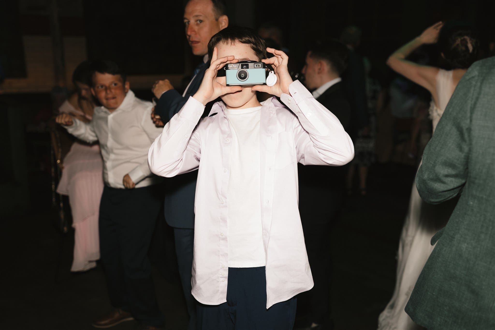 young wedding guest holds up a teal blue disposable film camera at the wedding reception