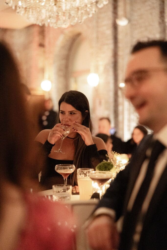 Guest sipping a cocktail beneath the chandeliers during a winter wedding cocktail hour