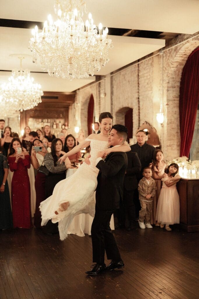 Bride and groom laughing as he lifts her during their first dance at the wedding reception