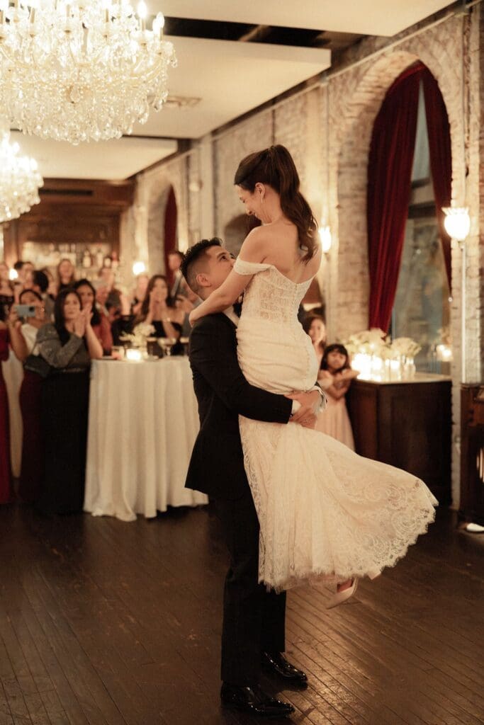 Groom lifting his bride during their first dance beneath crystal chandeliers at Cicala at The Divine Lorraine