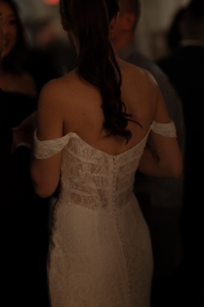 Detail of the bride's off-the-shoulder lace wedding dress with a covered-button back