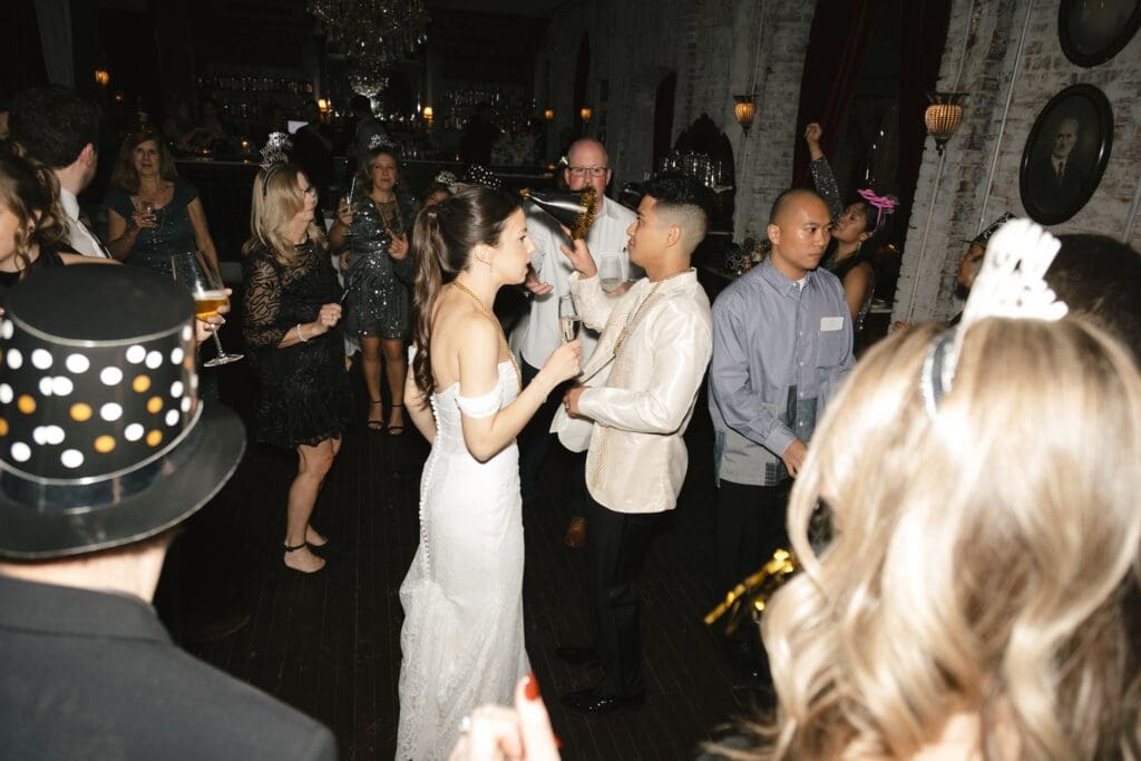 Bride and groom toasting at midnight as guests celebrate in Happy New Year hats at their winter wedding