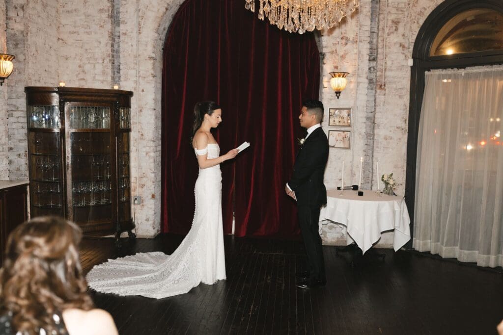 Bride reading her vows, her long lace train pooled across dark wood floors at the Divine Lorraine venue