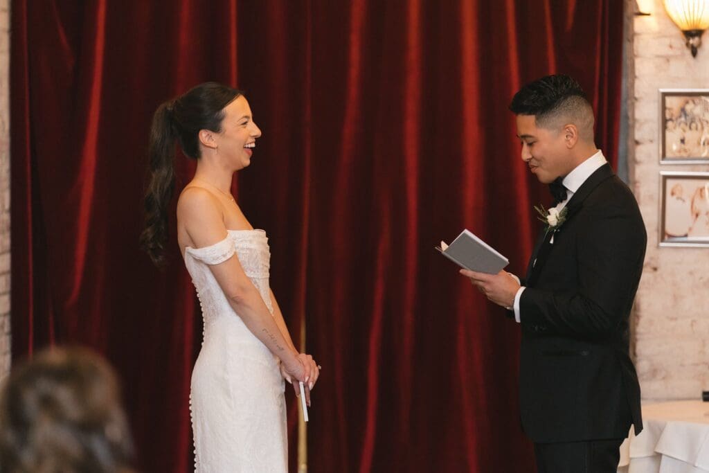 Bride and groom exchanging vows against a deep red velvet backdrop