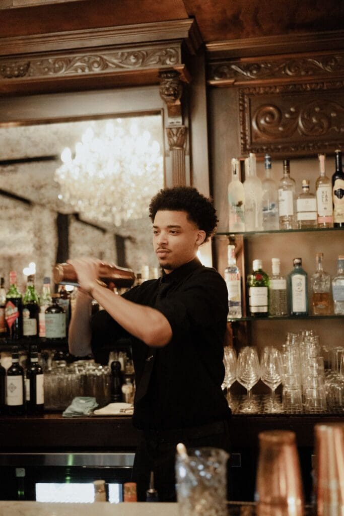 Bartender shaking a cocktail behind the carved wood bar at Cicala at The Divine Lorraine