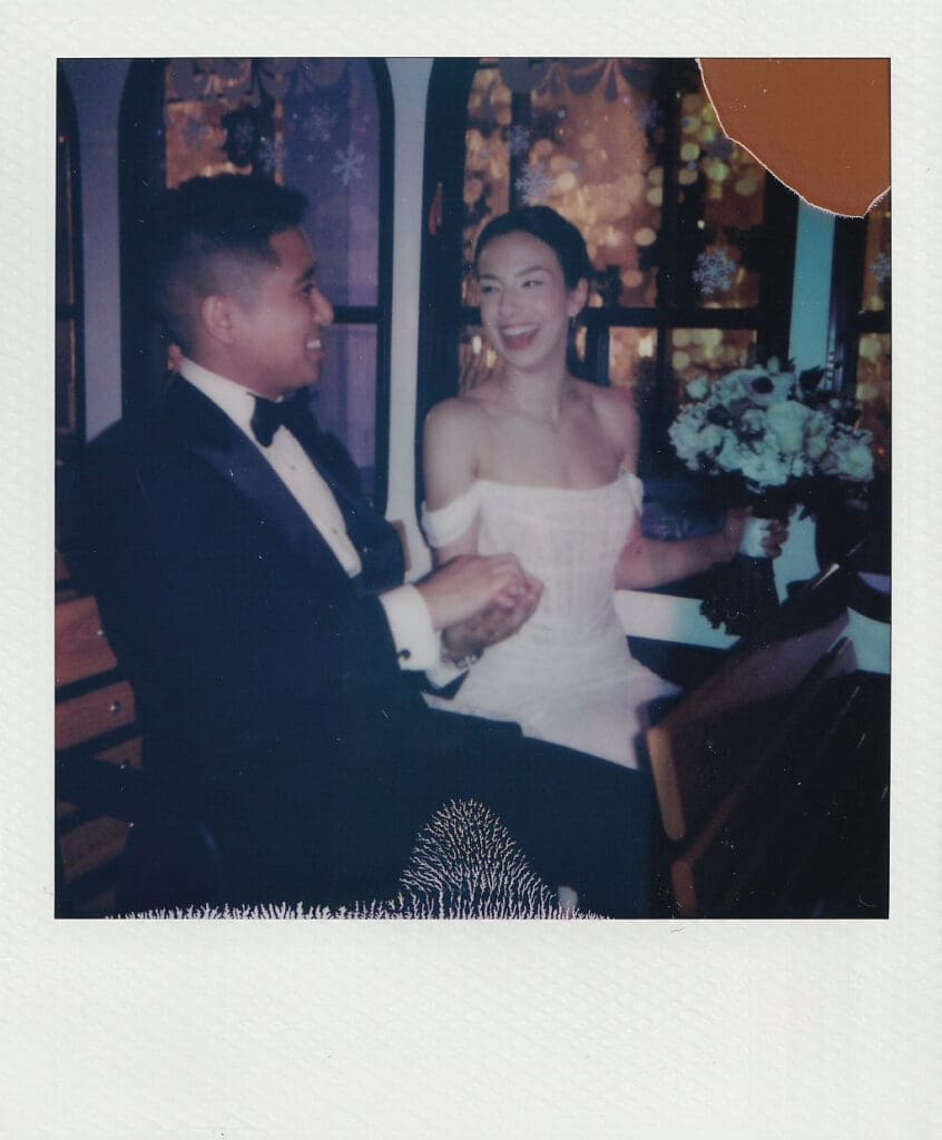 Film Polaroid of the bride and groom laughing, snowflake windows glowing behind them