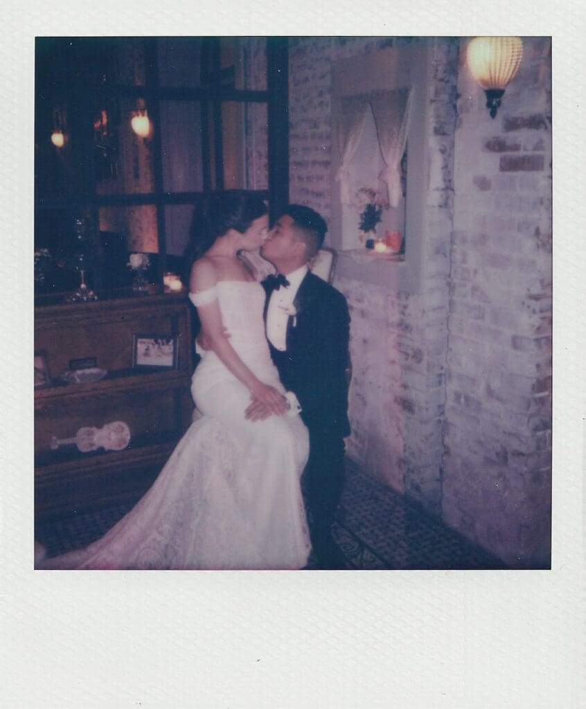 Film Polaroid of the newlyweds kissing in a candlelit, exposed-brick corner