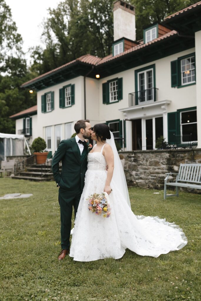 Bride and groom kiss in front of a venue designed in Spanish revival style architecture