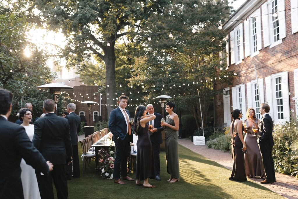 Wedding guests mingle in a courtyard under handing market lights behind Powel House, a historic Philadelphia wedding venue