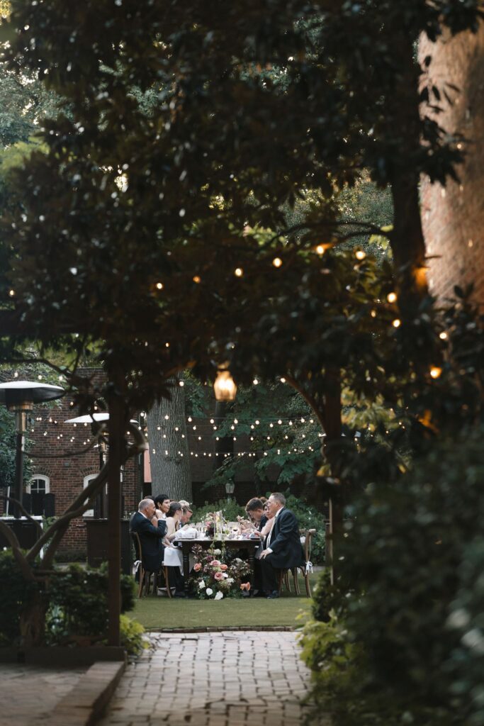 Guests are seated at a long banquet table under cafe lights for a backyard wedding at a unique Philadelphia wedding venue, Powel House