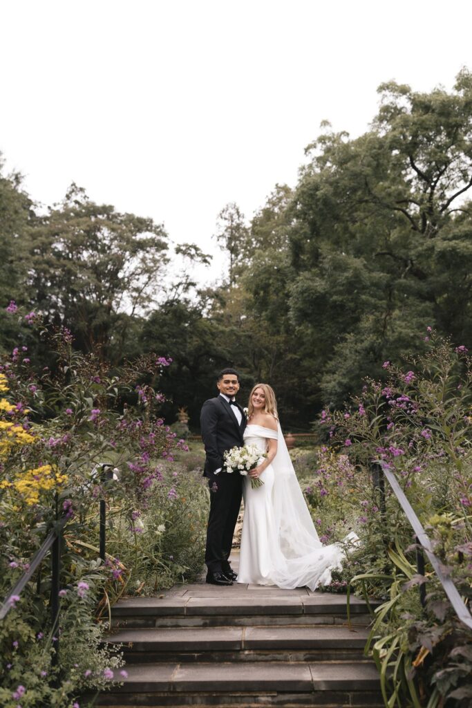 Bride and groom stand at the top of a stone stairwell surrounded by flowering bushes at Morris Arboretum, a historic Philadelphia wedding venue