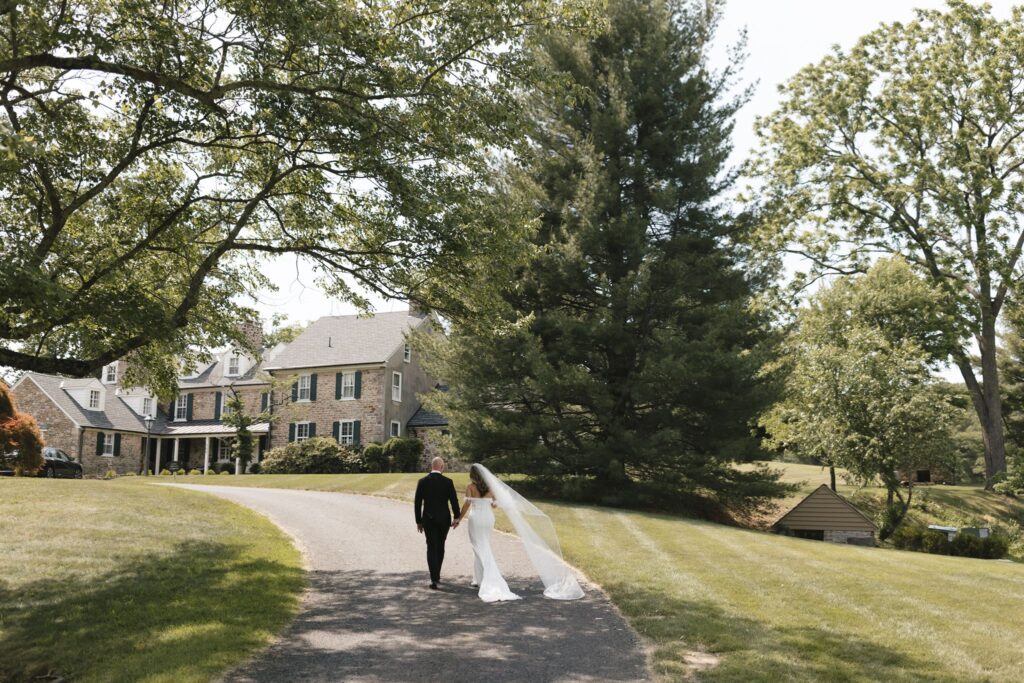 Bride and groom walk hand in hand towards the Inn at Fox Briar Farm, a historic wedding venue in Philadelphia
