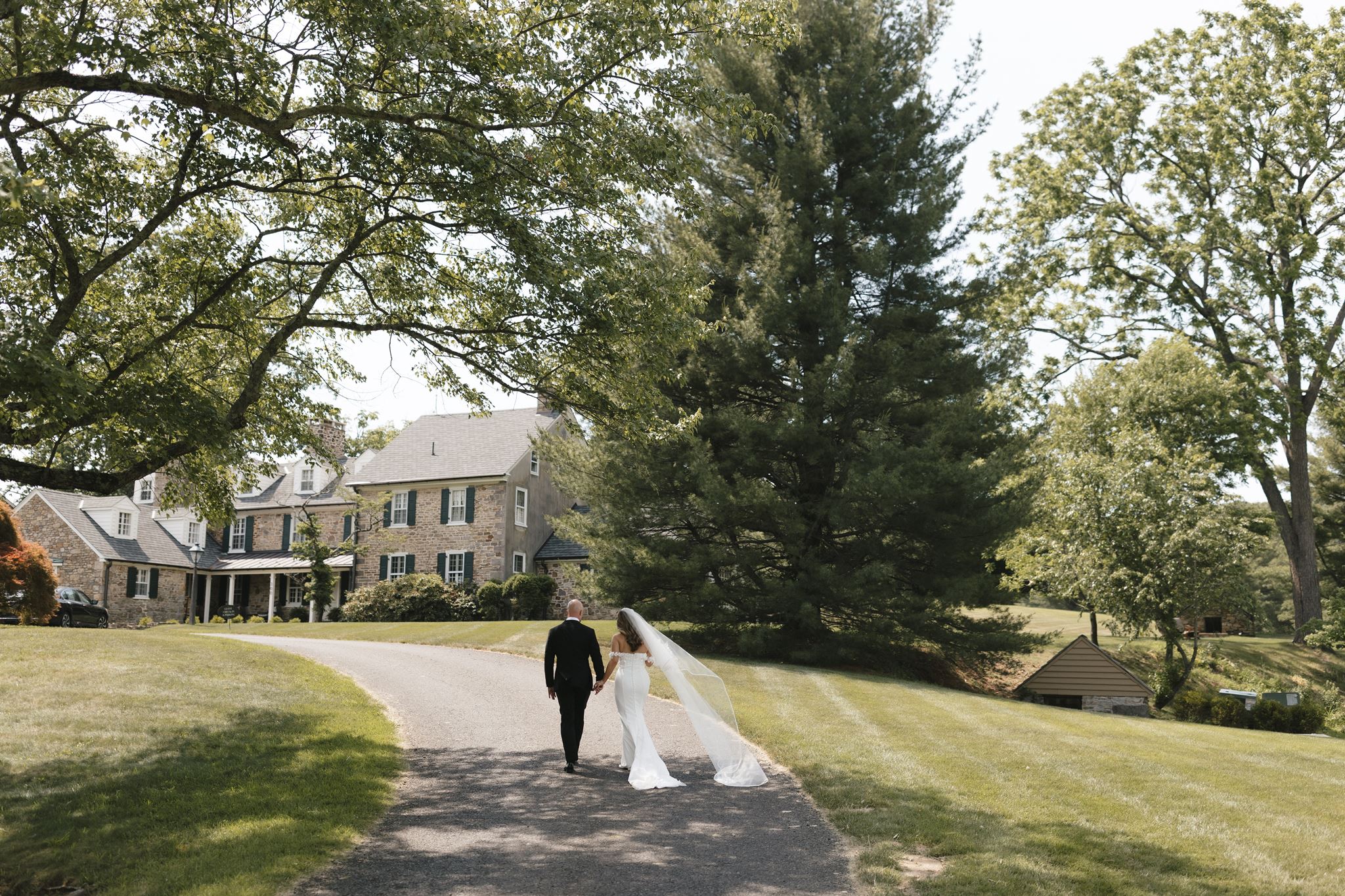 Bride and groom walk hand in hand towards the Inn at Fox Briar Farm, a historic wedding venue in Philadelphia