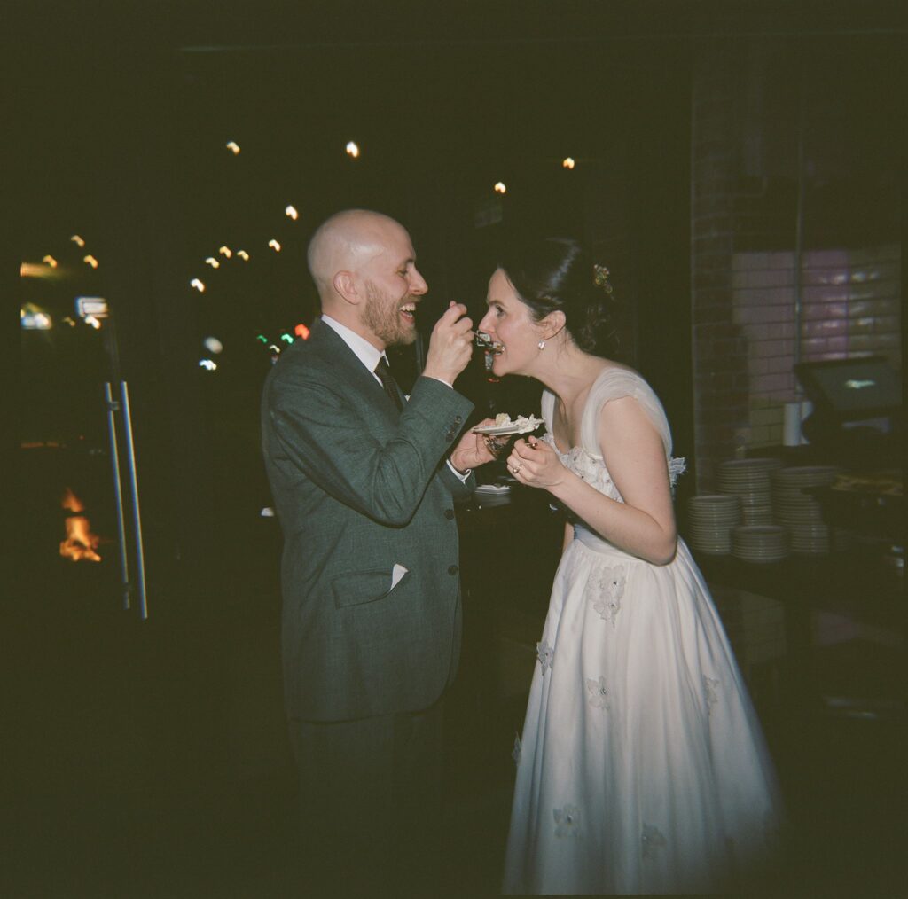 Film scan of groom laughing while feeding bride a bite of cake from a small plate