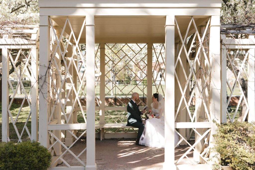 Groom reads vows from a small book to his bride under a pergola in the 18th Century Garden in Philadelphia's Old City