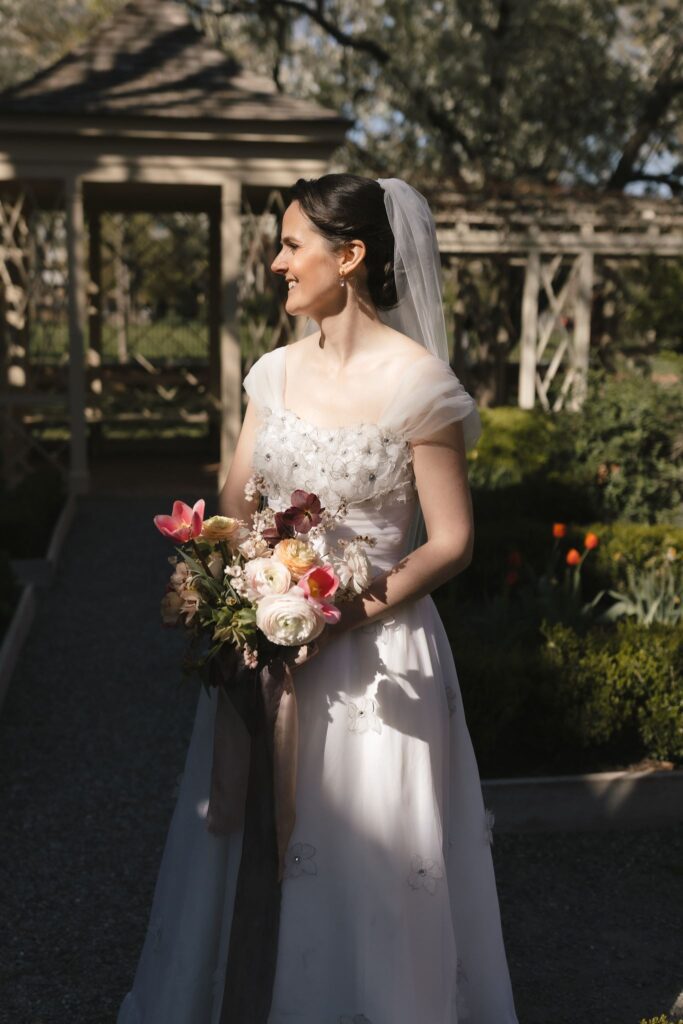 Bride holding pink and white bouquet stands in late afternoon sunlight in 18th Century Garden in Philadelphia's Old City