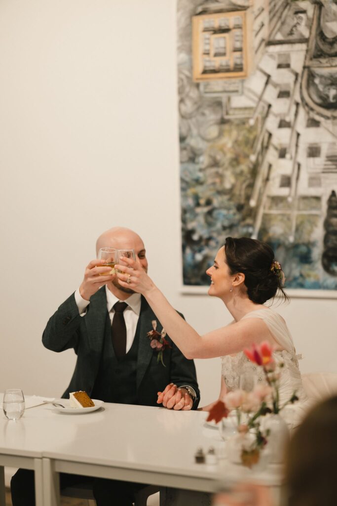 Bride and groom clink glasses full of white wine during their micro wedding at Frieda in Philadelphia