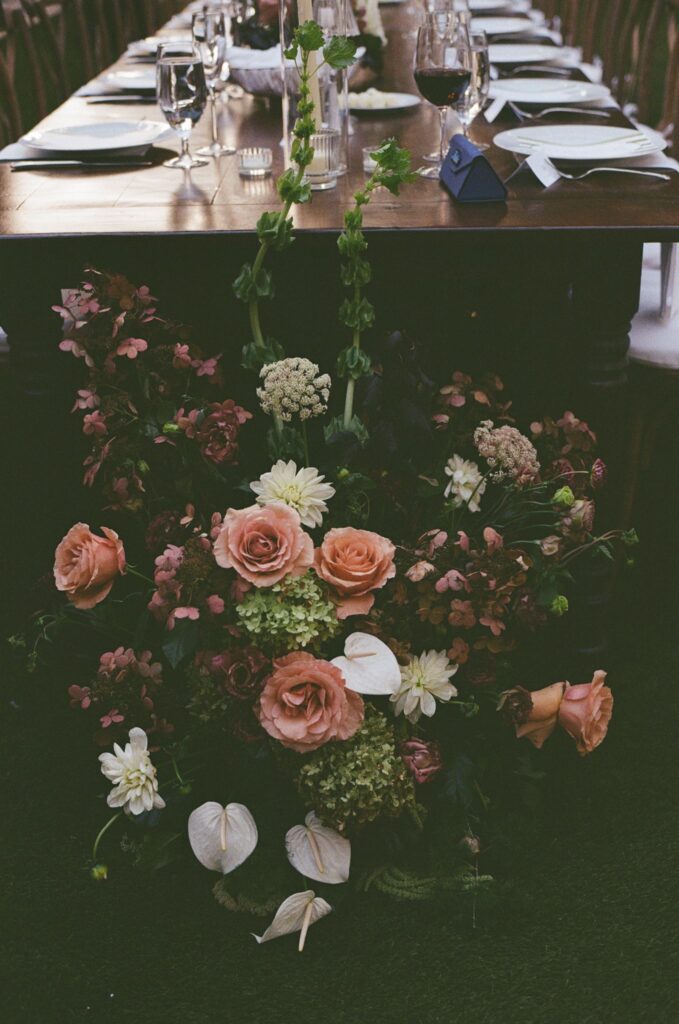 Warm pink and burgundy toned fall floral arrangement sits at the foot of a long banquet table during a backyard September wedding at the Powel House in Philadelphia