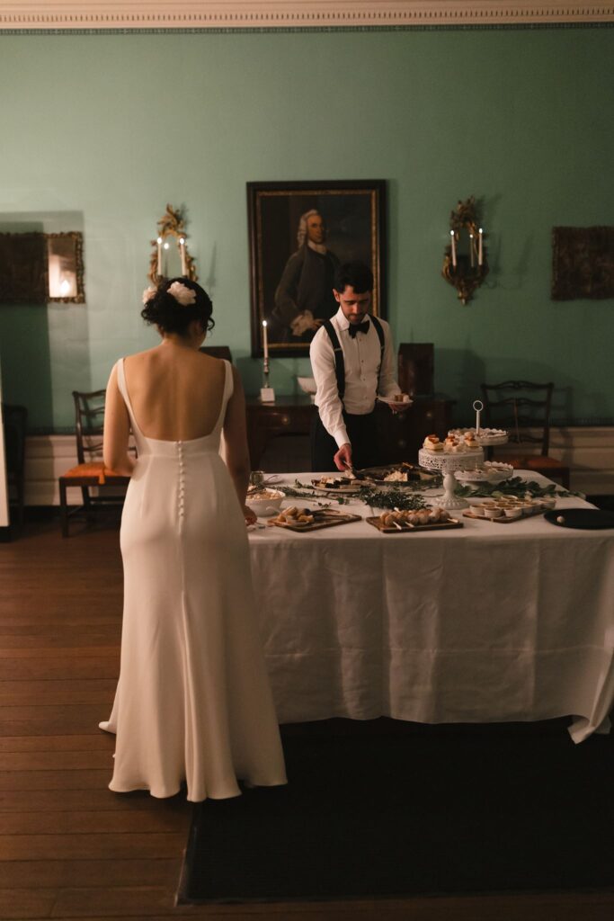 Bride and groom serve themselves small bites from a table filled with hors d'oeuvres in a mint green room at the Powel House in Philadelphia