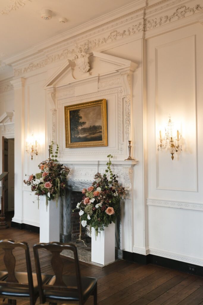Gold framed landscape oil painting it hung above an ornate mantlepiece flanked by two fall wedding floral arrangements for a wedding ceremony at Powel House in Philadelphia 