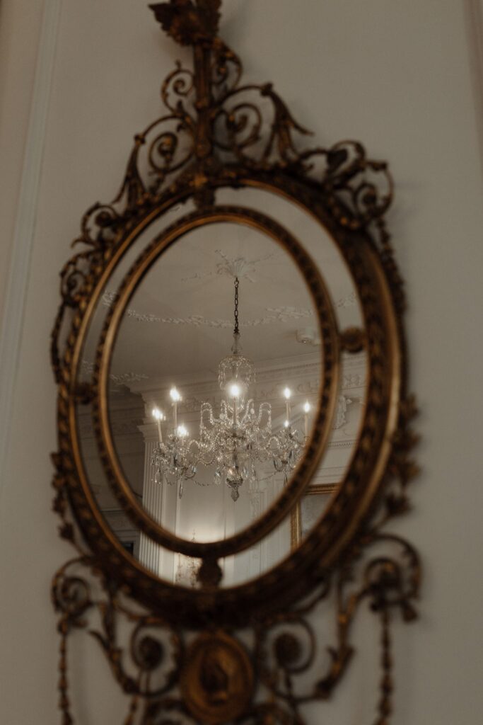 18th Century gilded mirror reflects an ornate crystal chandelier and carved ceiling at the Powel House in Philadelphia