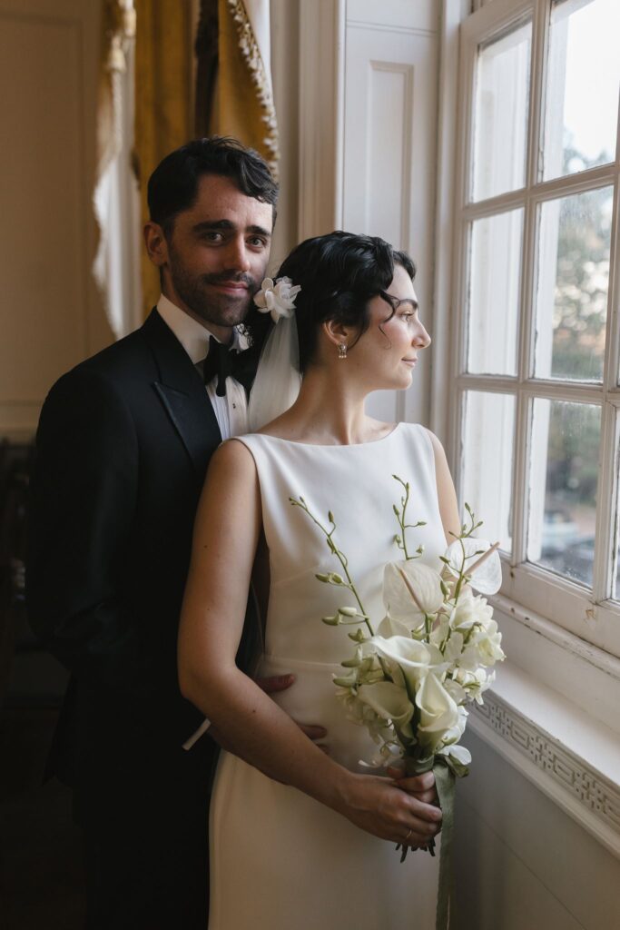 Bride and groom pose for a formal portrait by a window at the Powel House wedding venue in Philadelphia